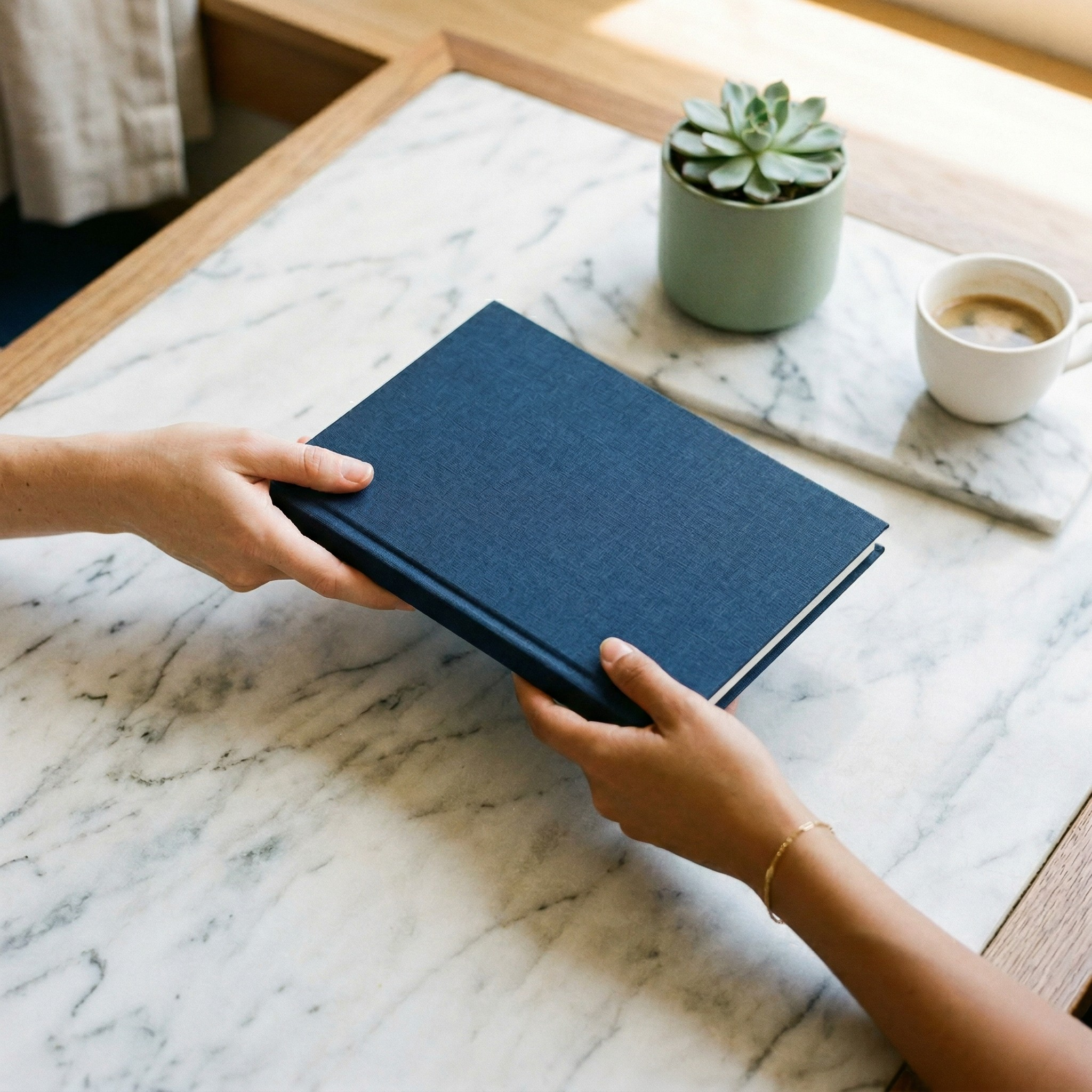 Hands exchanging a navy linen notebook over a marble table — representing the careful handoff of a vetted EA